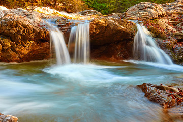 Beautiful waterfall in forest at sunset. Autumn landscape, fallen leaves, water flow 
