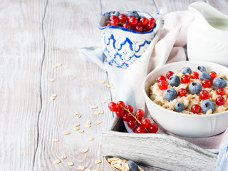 Wooden background with bowl of porridge, berries and milk