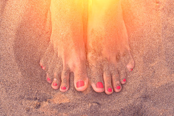Female feets with pink nails on the sand in the sunlight