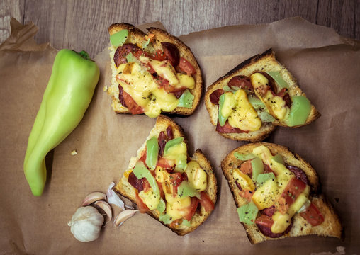 Bruschetta sandwitches with  garlic, cheese, tomatoes and peppers on a brown paper and wood.