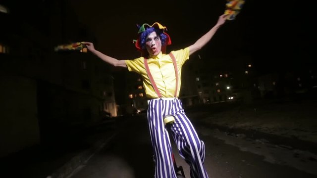 Sad scary clown riding on unicycles in a dark street. HD.