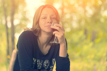 Blonde woman in black top holding a glass of red wine against a blurred background of green trees