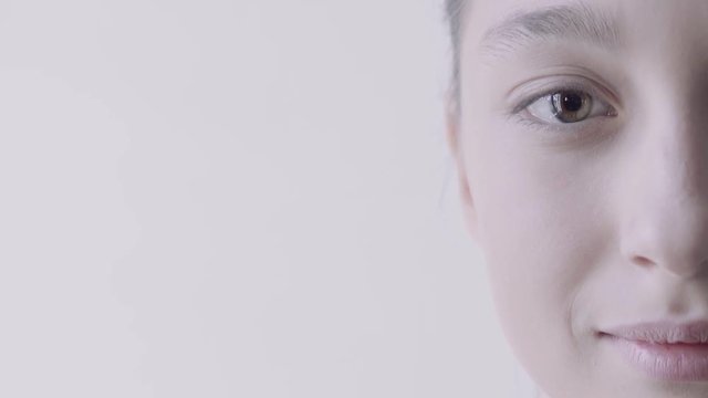 Close up of young mixed race woman looking in camera and smiling. Light grey background.