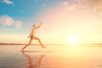 Fototapeta na wymiar Adult man with a mohawk on his head and black shorts running on water against the backdrop of blue sky with clouds in the sunlight