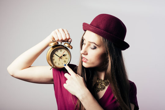 Portrait of elegant beautiful young lady in hat showing alarm clock