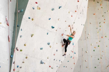 Gordijnen Sporty young woman exercising in a colorful climbing gym © EdNurg