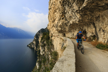 Fototapeta premium Mountain biking at sunrise man over Lake Garda on path Sentiero