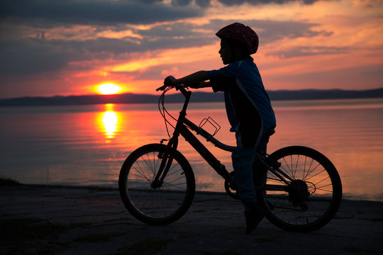 Silhouette of a young boy, at sunset, riding bicycle