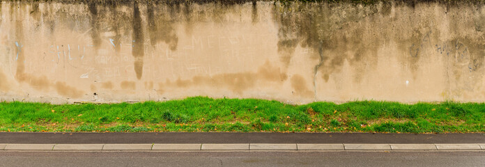 Panorama Hintergrund aus Mauer mit hellem Putz mit Wasserflecken und Boden aus Asphalt und Gras -...