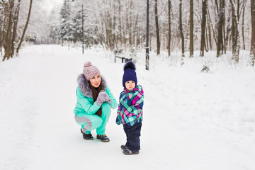 Fototapeta na wymiar happy mother and baby girl on the walk in winter snowy forest