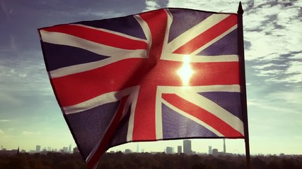 British Union Jack flag flying in front of a sunrise skyline of London, England