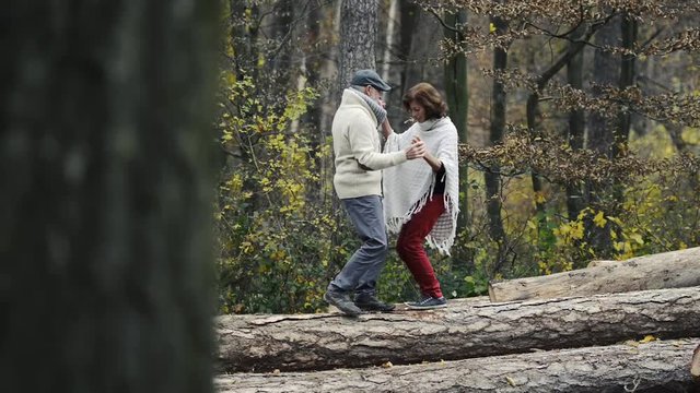 Senior couple in autumn forest walking on wooden logs