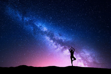 Milky Way with silhouette of a standing woman practicing yoga on the mountain. Beautiful landscape with meditating girl against night starry sky with milky way. Amazing galaxy. Universe. Travel 