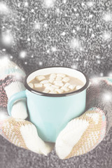 Girl keeps a mug of hot cocoa with marshmallows in mittens. Toni