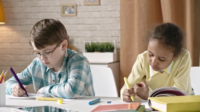 Boy and girl sitting at the table at home and drawing with felt tip pens