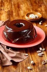 Marble Pistachio, Chocolate and Vanilla Cake (whole) covered with chocolate glaze, on red plate and brown wooden table.