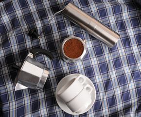 Geyser coffee, grinder and white cups on blue plaid texture