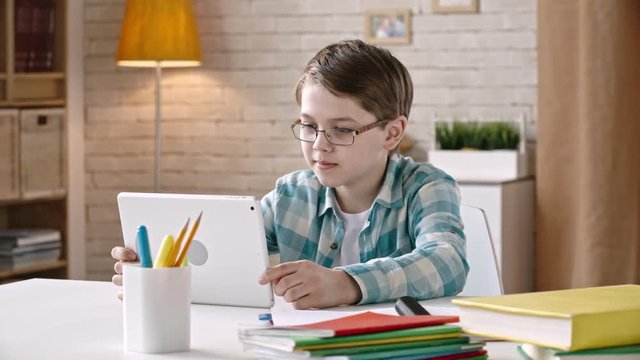 Little boy using tablet for talking via video call while sitting at desk at home