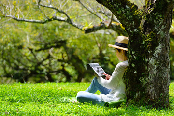 Happy middle aged woman sitting on green grass using tablet computer in the park