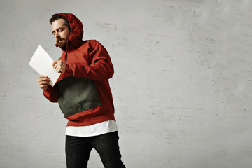 A fashionable male model in jeans, white t-shirt and red and grey parka reading something on a white blank sheet of paper isolated on white © BublikHaus