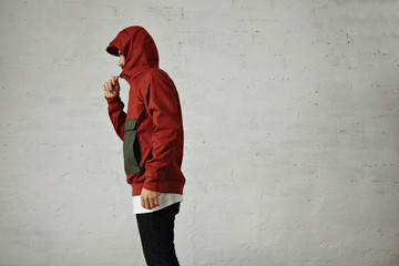 A serious looking young man zips up his fashionable red and grey anorak, shot from the side isolated on white © BublikHaus