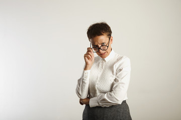 Angry crazy looking teacher adjusting her round black glasses against white wall background