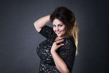 Young beautiful plus size model in black lace dres, xxl woman portrait on gray studio background