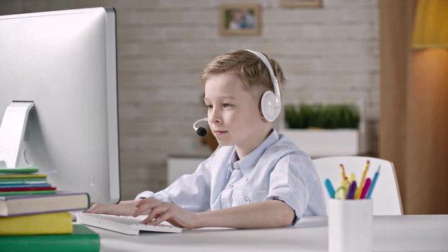 Young boy sitting with headphones and mic and having video call on computer