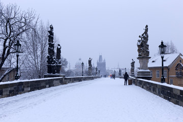 Snowy foggy Prague Old Town with Bridge Tower and St. Francis of Assisi Cathedral from Charles Bridge with its baroque Statues, Czech republic
