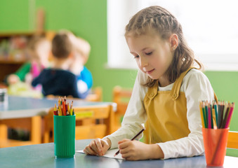 Little girl drawing with pencil in kindergarten.