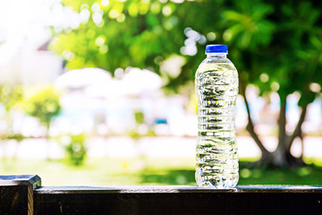 Plastic bottle with water standing on a summer, trees and pool on a background.