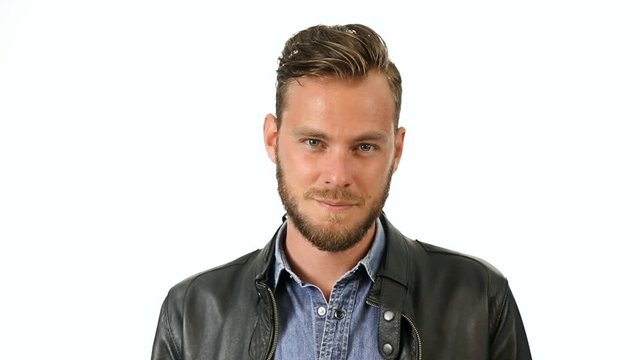 A handsome man wearing a black leather jacket and jeans shirt moving in front of a white background smiling.