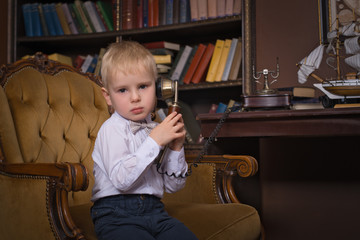 A very serious little boy wearing a white shirt and bow tie talking on a retro phone