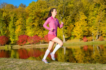 Woman running in autumn park, beautiful girl runner jogging outdoors, training for marathon, exercising and fitness concept
