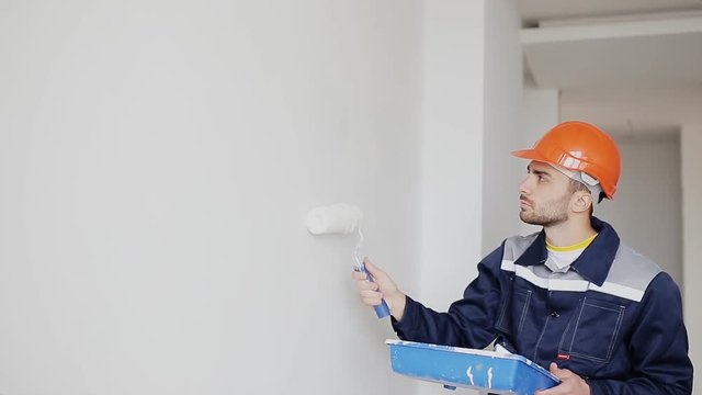 Young man paint wall in white. Brush or roller with white paint.