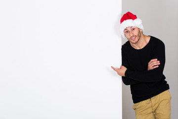 junger Mann mit Weihnachtsmann Mütze präsentiert an weißer Wand