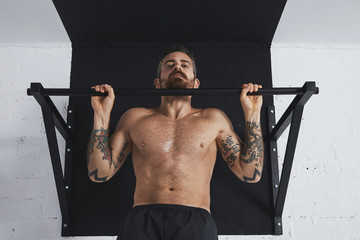 Fototapeta na wymiar Strong tattooed topless male athlete shows calisthenic moves close up of classic pullup hold in top bar