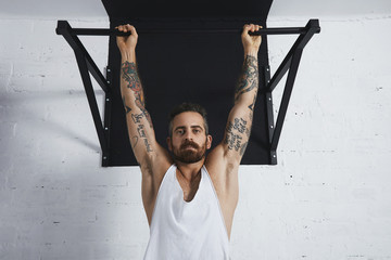 Brutal tattooed athletic man in white unlabeled tank t-shirt shows calisthenic moves close up of...