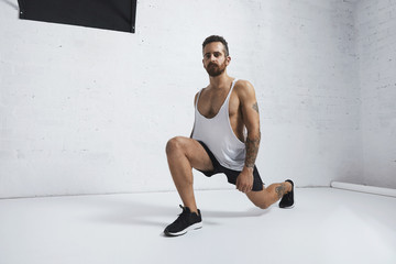 Strong tattooed in white unlabeled tank t-shirt male athlete shows calisthenic moves Lunges,...
