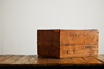 Brown rustic wooden wine box with barely legible black letters on a wooden table against white wall...