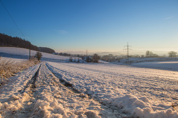 Fototapeta na wymiar Winterlandschaft mit Oberleitungen für Strom im Gegenlicht bei blauem Himmel