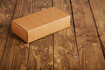 Craft unlabeled cardboard package box presented on stressed brushed wooden table, closeup