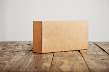 Craft unlabeled cardboard package box presented on stressed brushed wooden table, isolated on white...