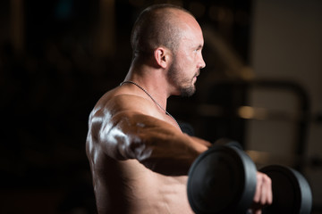 Fototapeta na wymiar Muscled Male Model Exercising Shoulders With Dumbbells