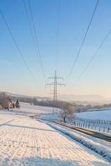 Winterlandschaft mit Oberleitungen für Strom im Gegenlicht bei blauem Himmel