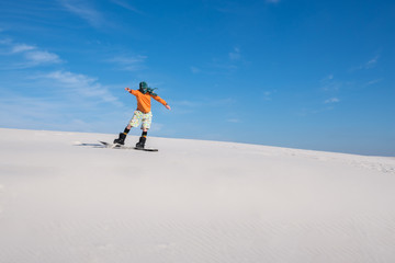 Naklejka na ściany i meble Snowboarder, wearing a scarf rides on sand dune