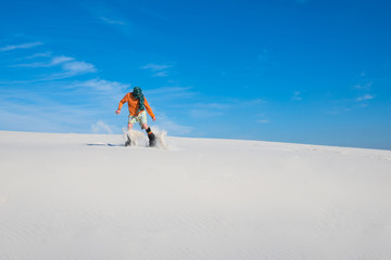 Naklejka na ściany i meble Snowboarder, wearing a scarf landing after jump on a sand dune