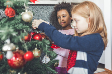 African and redhead little girls decorating the Christmas tree. Natural light. 