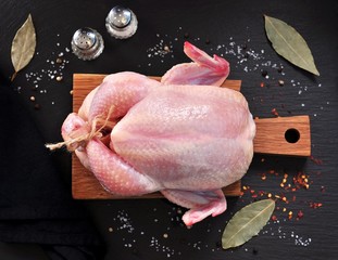 Raw chicken with spices on a wooden board on a black stone.