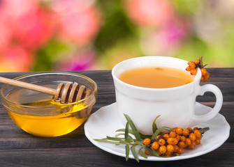 Tea of sea-buckthorn berries with honey on wooden table  blurred garden background